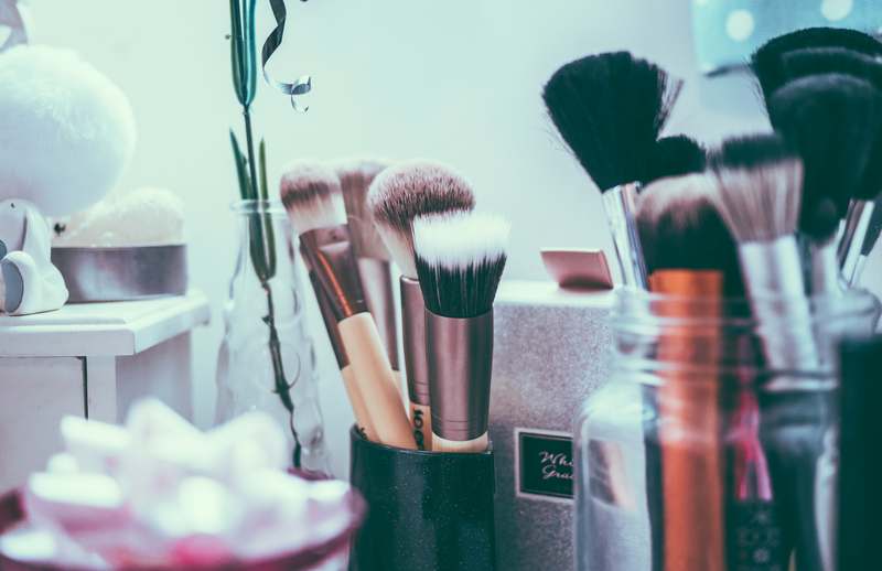 Diverse group of makeup artists collaborating around a lighted vanity table with brushes, palettes, and skincare products visible